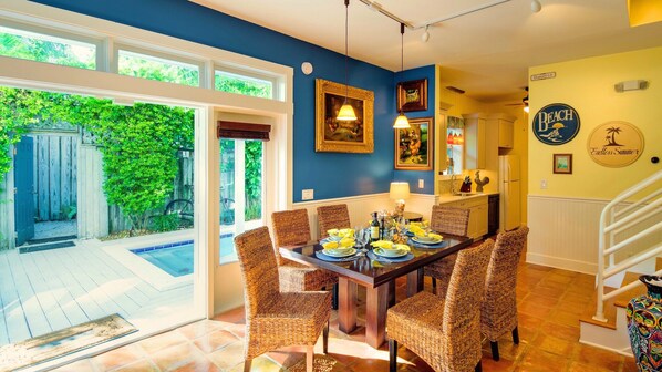 A dining area with wicker chairs, a wooden table set for four, and a view of a backyard with a wooden fence and greenery. - **SWEET AMERICANA** 8BR/8BA Compound & 2 Pools + Last Key White Glove Service... (Key West)