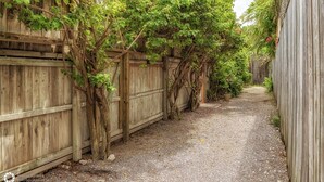 Un étroit sentier de gravier bordé de clôtures en bois recouvertes de plantes grimpantes.