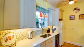 A kitchen with white cabinets, a sink, a dishwasher, and a window with decorative hanging lights. - **SWEET AMERICANA** 8BR/8BA Compound & 2 Pools + Last Key White Glove Service... (Key West)