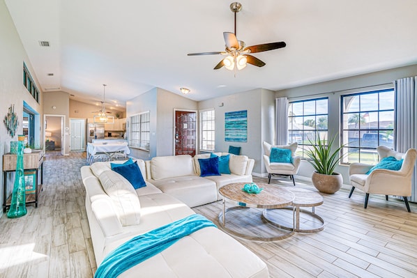 A spacious living room with a large white sofa, a round coffee table, and a ceiling fan.