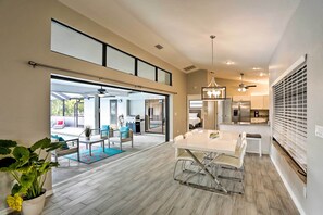 A spacious living area with a large dining table, a ceiling fan, and a view into the adjacent room.