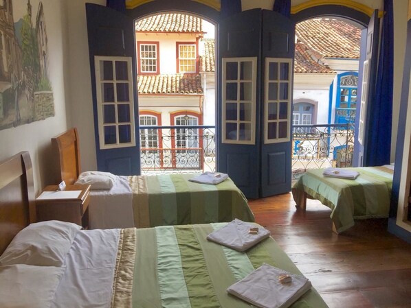Habitación de hotel con dos camas, una mesita y vista a un edificio desde una puerta abierta.