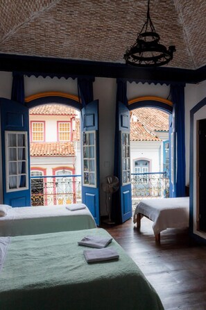Habitación con dos camas, un ventilador y vistas a edificios desde puertas abiertas.