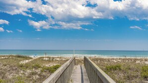 A wooden boardwalk leading to a beach with a clear sky and ocean view.