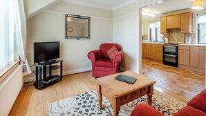 A living room with a TV, red armchair, wooden coffee table, and a patterned rug. - 1 bedroom accommodation in Horsford, near Norwich (Horsford, near Norwich)