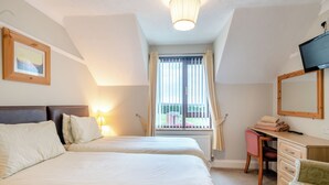 A bedroom with two beds, a desk, a chair, a television, and a window with curtains. - 1 bedroom accommodation in Horsford, near Norwich (Horsford, near Norwich)