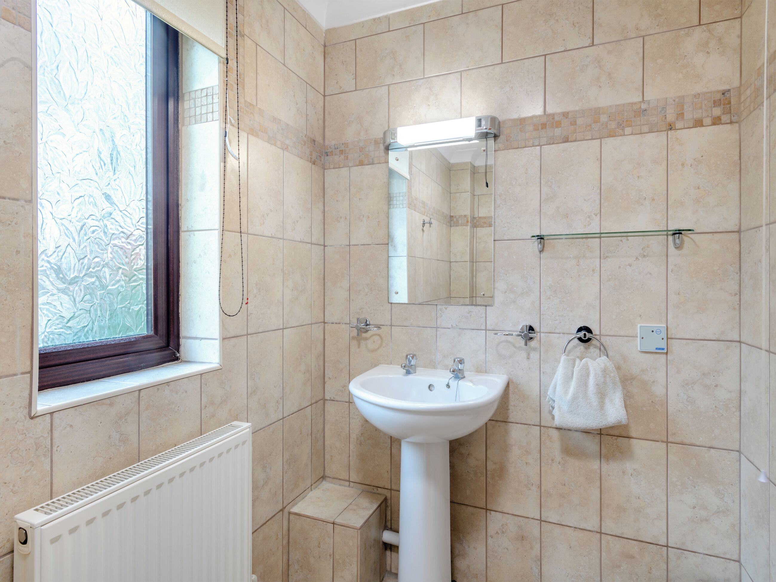 A bathroom with a white sink, a mirror above it, a towel hanging on a rack, and a window with frosted glass.
