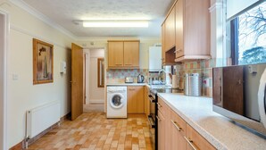 A kitchen with wooden cabinets, a washing machine, a countertop with a kettle, and a window with a view. - 1 bedroom accommodation in Horsford, near Norwich (Horsford, near Norwich)