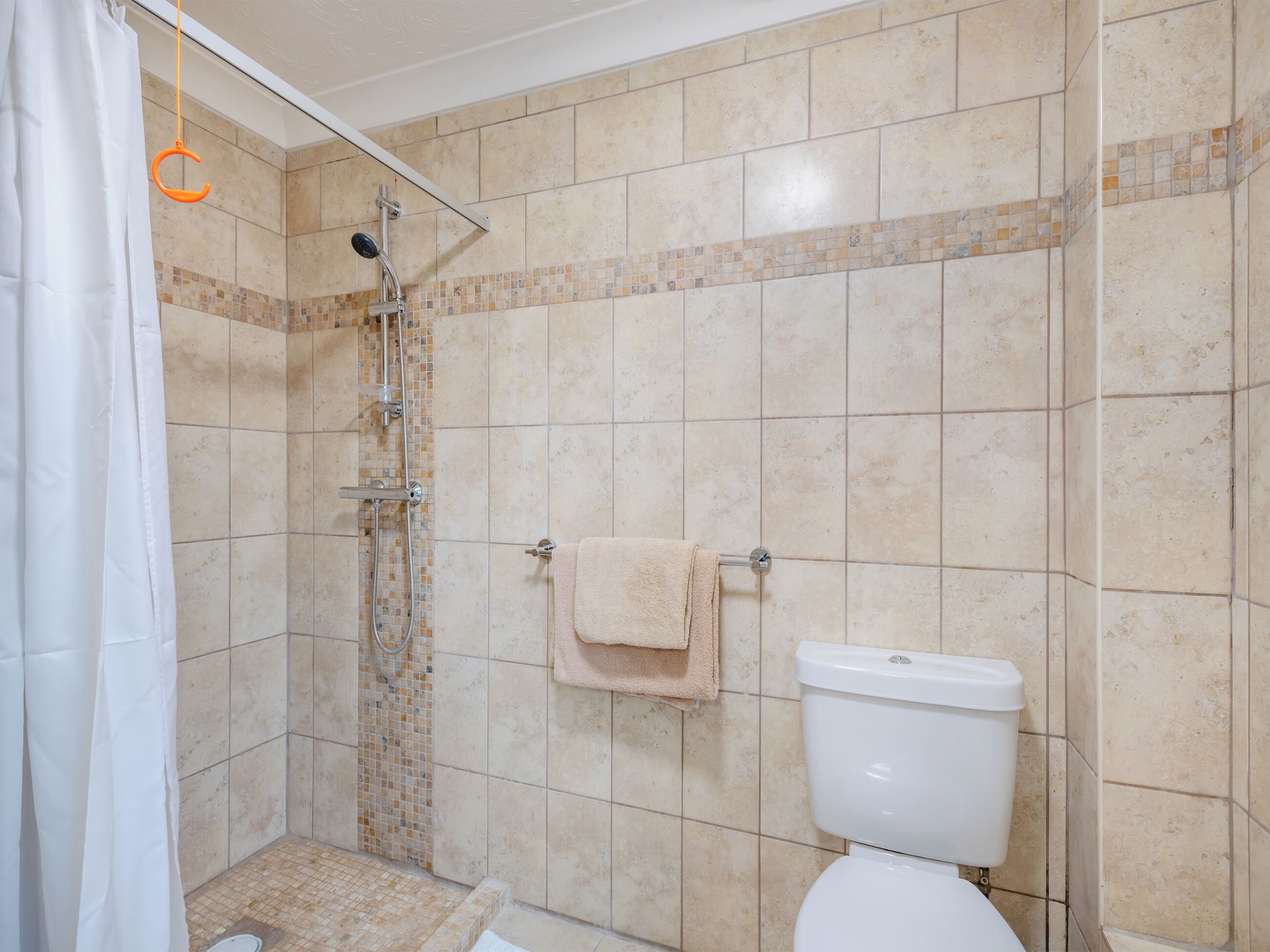 Een badkamer met een douche, toilet en betegelde wanden.
