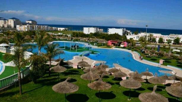 A resort with a large pool, palm trees, and a view of the ocean. - Apartment in Jawhara2 Marina Smir next to the beach with pool. (Tetuán)