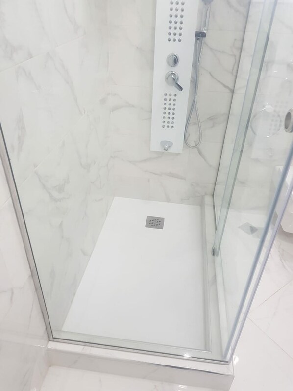 A glass-enclosed shower stall with a control panel and a handheld showerhead.