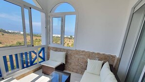 A balcony with a glass table and dark wicker furniture, overlooking a landscape with buildings. - Apartment in Jawhara2 Marina Smir next to the beach with pool. (Tetuán)