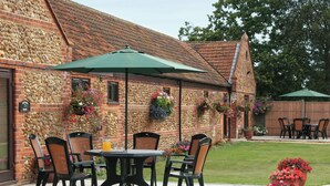 An outdoor patio with a brick wall, a table with chairs, and hanging flower baskets. - Littlewood Barn - UKC3737 (Foxley, near Fakenham)