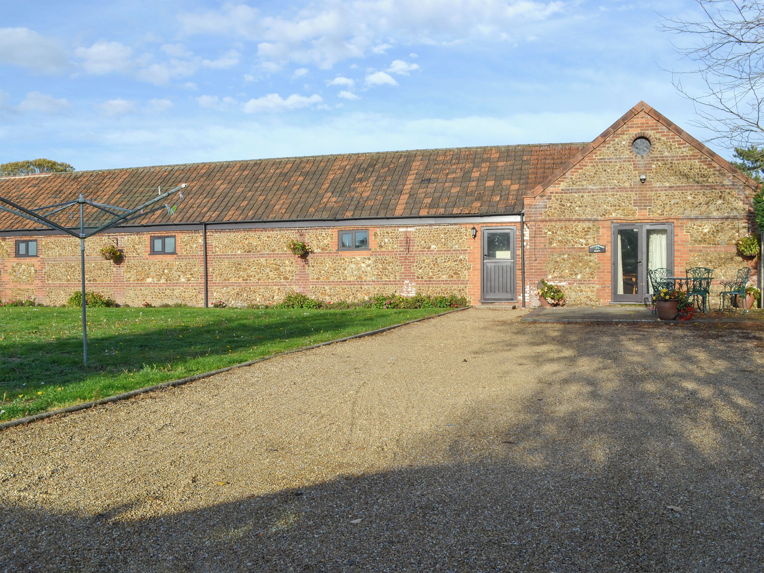 A stone building with a tiled roof, a gravel driveway, and a small garden area with potted plants.