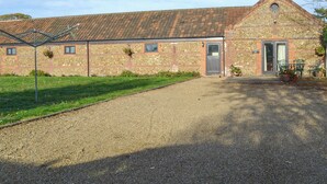 A stone building with a tiled roof, a gravel driveway, and a small garden area with potted plants. - Littlewood Barn - UKC3737 (Foxley, near Fakenham)