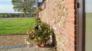 A brick building with a sign reading "Littlewoods Barn." There are flower pots with pink and white flowers along the wall. - Littlewood Barn - UKC3737 (Foxley, near Fakenham)
