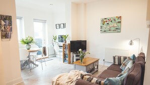 Un salon moderne avec un canapé marron, une table basse, un téléviseur et un coin repas comprenant une table et des chaises.