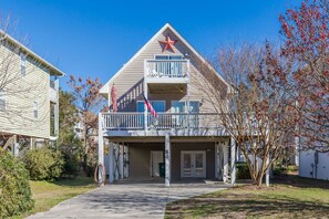 A two-story building with a balcony, a red star decoration, and a flag. - The Sea Urchin - Charming 4 Bedroom Coastal Home (Surf City)
