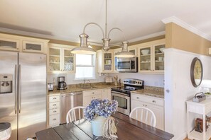 A kitchen with stainless steel appliances, white cabinetry, and a dining table with chairs. - The Sea Urchin - Charming 4 Bedroom Coastal Home (Surf City)
