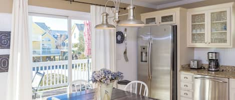 A kitchen with a stainless steel refrigerator, a coffee maker, and a dining area with a wooden table and chairs.