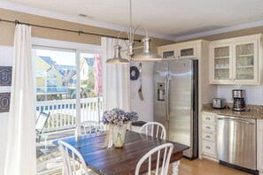 A kitchen with a stainless steel refrigerator, a coffee maker, and a dining area with a wooden table and chairs.