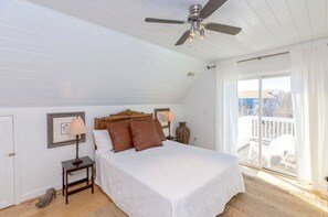 Une chambre à coucher avec un lit, deux lampes de chevet, un ventilateur de plafond et une vue sur l’extérieur.