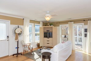 A living room with a white sofa, a television, a ceiling fan, and a view of the outdoors. - The Sea Urchin - Charming 4 Bedroom Coastal Home (Surf City)
