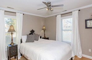 A bedroom with a bed, two bedside tables with lamps, a ceiling fan, and a clock on the wall. - The Sea Urchin - Charming 4 Bedroom Coastal Home (Surf City)