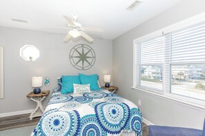 A bedroom with a bed, a ceiling fan, a window with blinds, and a wall-mounted compass decoration.