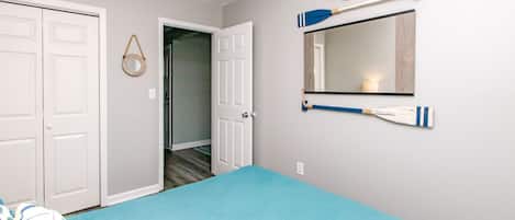 A bedroom with a bed, a door, a mirror, and a wall decoration.