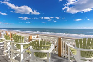 A deck with green chairs overlooking a beach.