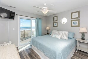 Une chambre avec un lit, un ventilateur de plafond, un téléviseur fixé au mur et une vue sur l’océan par une porte coulissante.