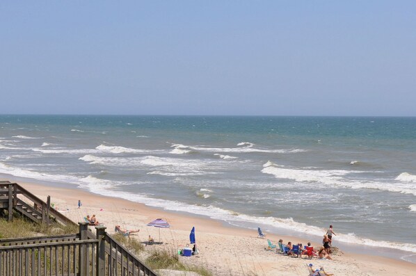 A beach with a wooden boardwalk leading to the shore, where people are sunbathing and relaxing.
