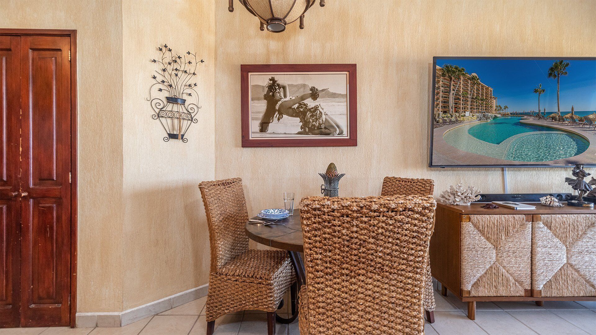 A dining area with wicker chairs, a wooden table, and a painting of a tropical beach scene.