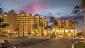 A multi-story hotel with a central courtyard, palm trees, and a sunset sky. - Sonoran Sea W-109 Serenity By The Sea Bright Oceanfront Condo (Puerto Peñasco)