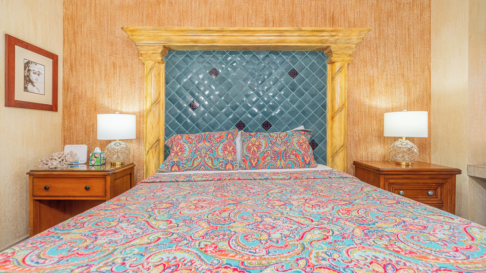 Una habitación de hotel con una cama grande, dos mesitas de noche, un cabecero con diseño de rombos y un cuadro en la pared.