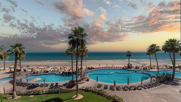 Un resort con una vasta area piscina, palme e vista sulla spiaggia.