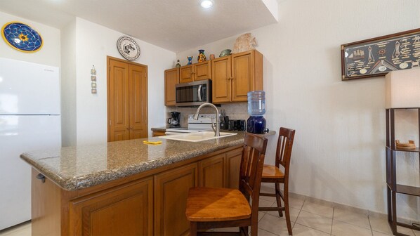A kitchen with wooden cabinets, a granite countertop, a built-in microwave, a sink, and a water dispenser.