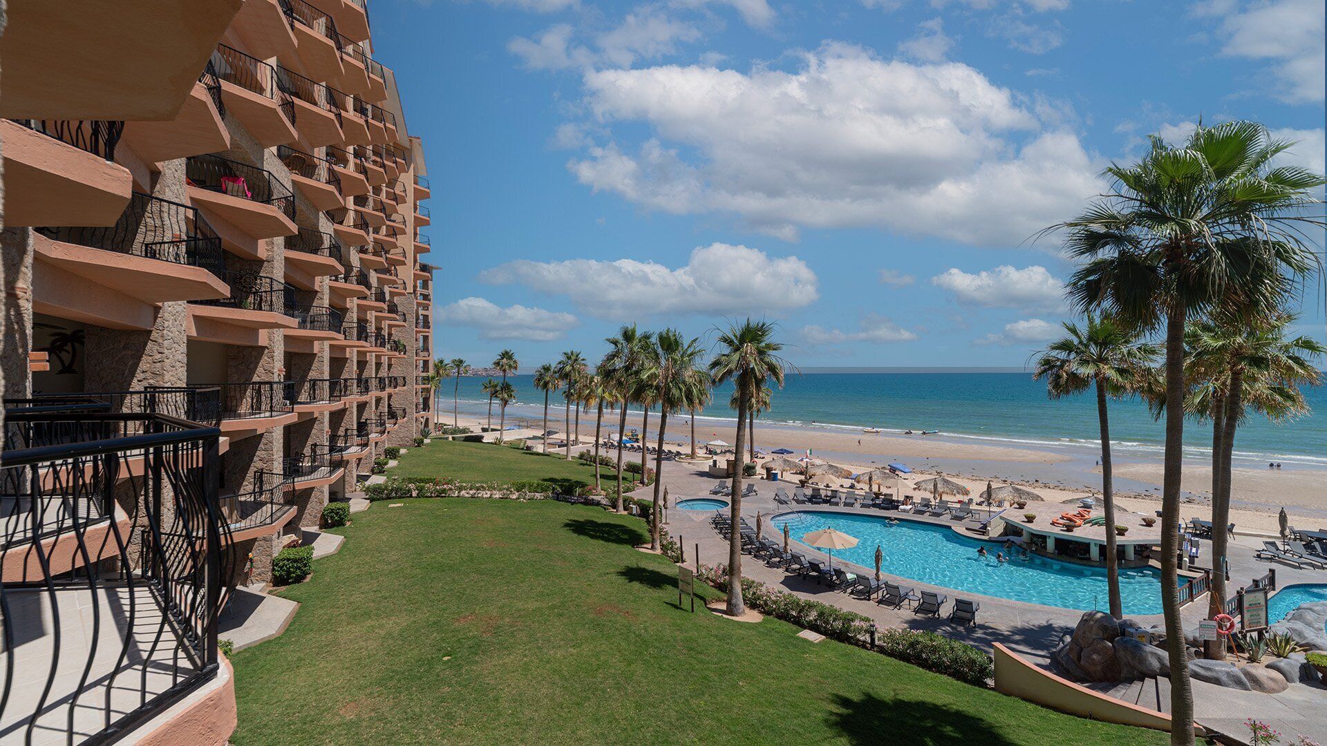 Un hotel con zona de piscina, palmeras y vistas a la playa.