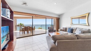 A spacious living area with a balcony overlooking the sea, a sofa set, and a bookshelf.