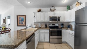 A kitchen with white cabinets, stainless steel appliances, a granite countertop, and a tiled floor.
