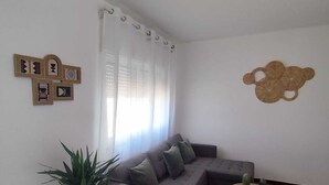 Una sala de estar con un sofá gris, una mesita redonda, una planta en maceta y obras de arte en la pared.