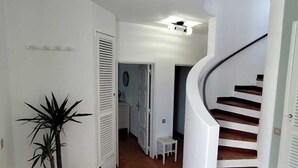 Un pasillo con piso de madera, una escalera blanca y una planta en maceta.