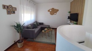 Un salón con sofá, una mesita redonda, una planta en maceta y un televisor instalado en la pared.