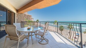 Un balcon avec une table et des chaises, donnant sur une plage et un bâtiment d’hôtel.