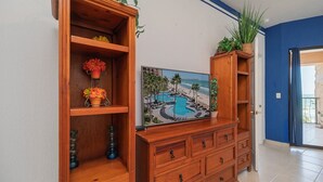 Un meuble en bois orné d’un tableau représentant une piscine et des palmiers, ainsi qu’une plante en pot et un vase de fleurs.
