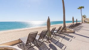 Eine Strandlounge mit Liegestühlen und Sonnenschirmen, Palmen und freiem Blick auf das Meer.