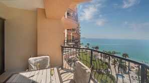 A balcony with a view of the sea, a table with chairs, and a glass of champagne.