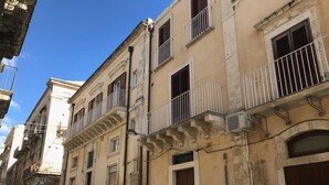 A narrow street lined with historic buildings, featuring balconies and a row of parked cars. - Elegant apartment, in the heart of the historic center of Noto, for 2 to 6 guests (Noto)
