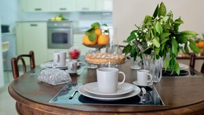A dining table with a white mug, a glass vase with green leaves, and a fruit bowl in the background. - Elegant apartment, in the heart of the historic center of Noto, for 2 to 6 guests (Noto)